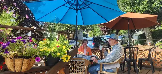 Customers sitting under a blue umbrella on the patio outside Blue Heron, beside pots of yellow flowers